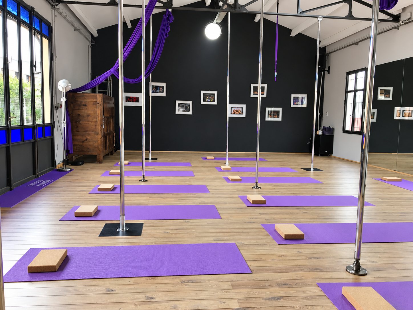 Vaste studio lumineux au parquet clair équipé de barres chromées, de tapis de yoga violets avec briques de liège et de tissus aériens violets.